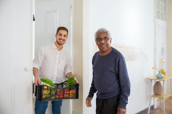Image représentant deux hommes debout souriants, l'un plus jeune tenant une caisse avec des légumes et l'autre plus âgé se tenant à côté de lui.